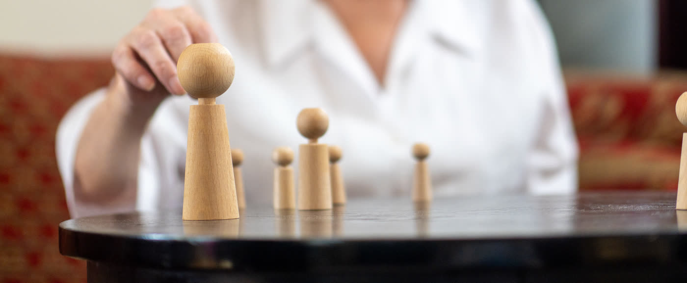 Eine Hand versetzt eine Holzfigur auf dem Tisch, daneben weitere Figuren für die systemische Aufstellung
