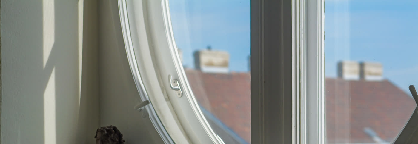 Blick durch das runde Fenster auf Dächer und blauen Himmel